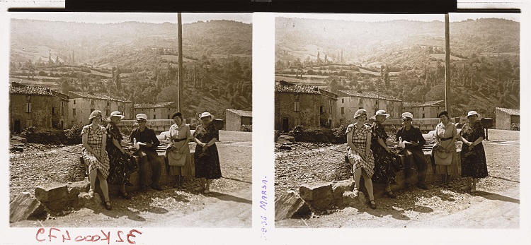 Quatre femmes et un homme assis sur un muret près du pont d’accès, le village en arrière-plan